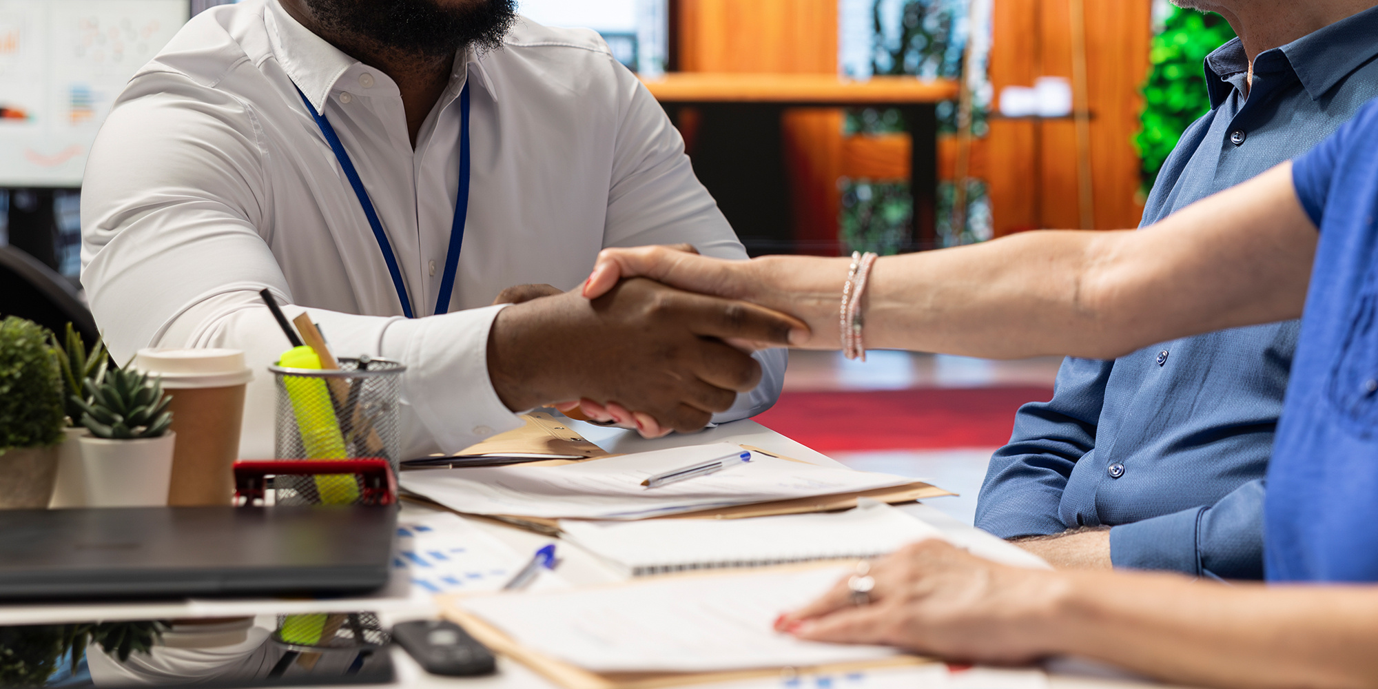 A Black man shakes a white woman's hand while another person sits nearby.